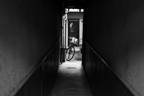 A grayscale of a corridor leading to bicycle parked in a backyard