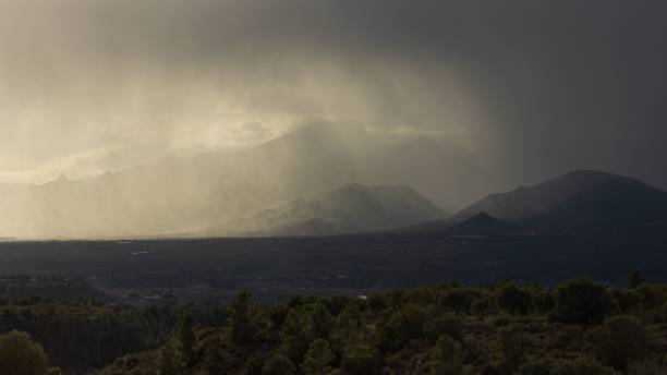 istock Dramatic shot of mountain silhouettes and fields under a cloudy sky with a heavenly effect 1444074912