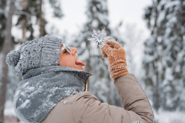 istock winter time Female dressed fashionable grey wearing sunglasses throws having fun, catching snowflakes with your tongue. 1444077230