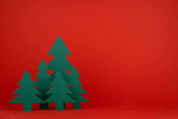 Bright Christmas background with paper green spruce forest on red backdrop in minimalist modern style, copy space. New year scene for presentation products and advertising text, card, poster, flyer.