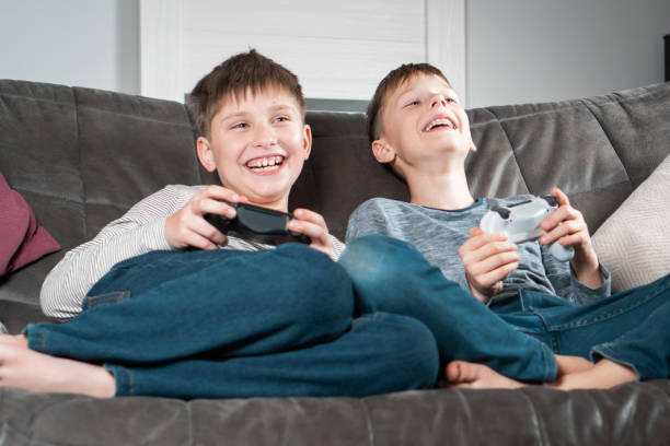 Portrait of two amazing barefoot teenage boys children sitting at home, holding gaming controller, playing videogames. stock photo