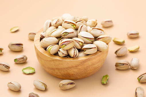 Pistachio nuts with shells in wooden bowl on pastel orange background