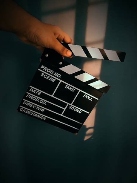 istock Vertical closeup of a hand holding a clapperboard with sunlight in the background. 1444087542