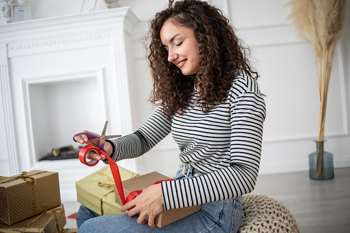One young woman, young woman wrapping gifts at home, happy and smiling while holding wrapping paper and gift box, approaching holiday or someone's birthday.