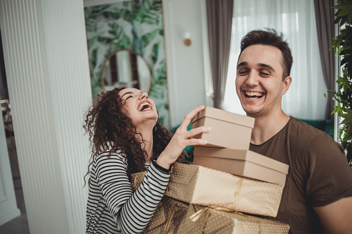 Male and female couple giving holiday gifts, happily enjoying their home on Valentine's Day or someone's birthday, dressed casually and smiling