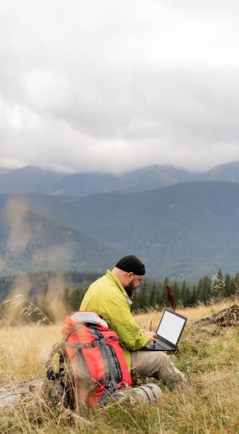 istock a bearded Caucasian man with a laptop sits on a fallen tree in the mountains with a beautiful view of the valley. 1444101416