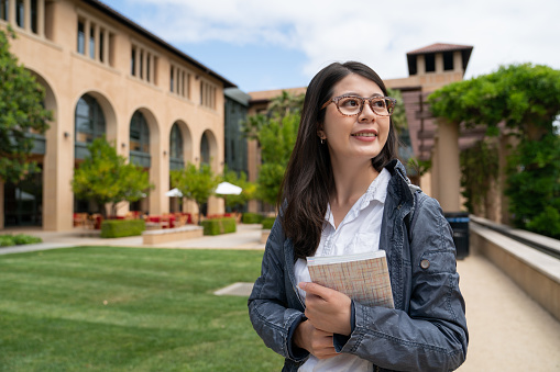 cheerful asian taiwanese female freshman student holding book feeling excited about her school life while sheâs on spring semester study abroad program at school university