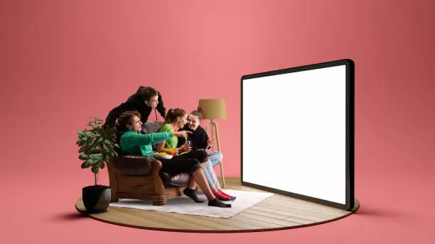 Photo of Happy young people, emotional friends watching football match, sport show or movie together. Youth sitting on sofa in front of huge 3D model of tv screen