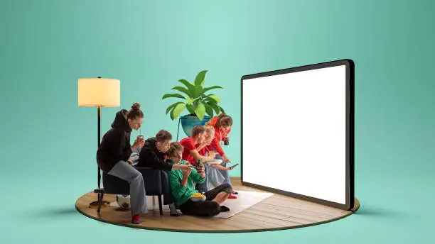 Photo of Make a choice. Young emotional friends, mates, students watching football match, sport show or movie together. Youth sitting on sofa in front of huge 3D model of tv screen