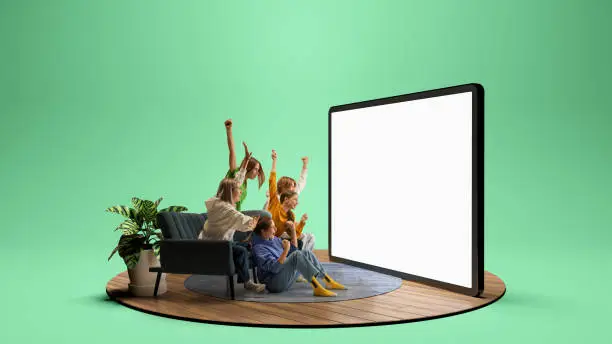 Photo of Group of young emotional friends watching football match, sport show or movie together. Excited girls and boys sitting in front of huge 3D model of device screen at home interior