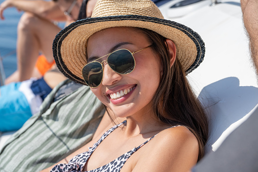 Portrait of smiling young woman wearing sunglasses sitting on boat deck during sunny day.
