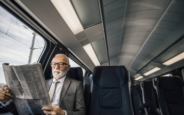 istock Senior businessman entrepreneur reading newspaper while sitting by window in passenger train. 1444107177