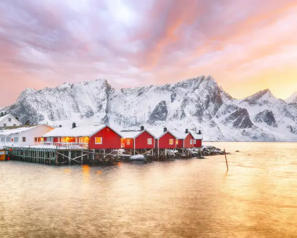 Traditional Norwegian red wooden houses (rorbuer) on the shore of Reinefjorden near Hamnoy village at sunset. Location: Hamnoy, Lofoten; Norway, Europe