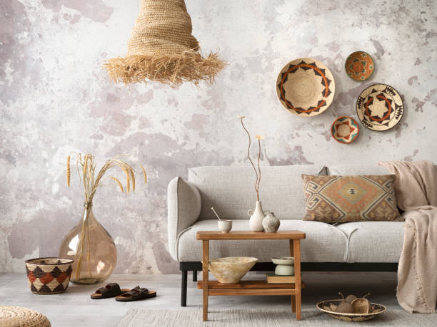 Interior design of ethnic composition living room interior with grey sofa, colorful wicker, boho straw lamp, gray concrete wall, bench and personal accessories. Home decor. Template.