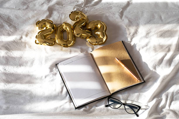 istock 2023 New year goals concept. Blank open notebook and foil balloons on white bedding. 1444109962