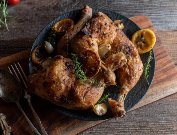 Homemade oven roasted crispy chicken legs. Marinated with thyme, lemon and garlic. Served hot and ready to eat on a dark plate isolated on wooden background from above.