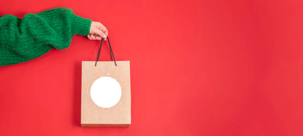 Xmas shopping concept. Woman's hand in green sweater holding a gift bag on a red background, stock photo
