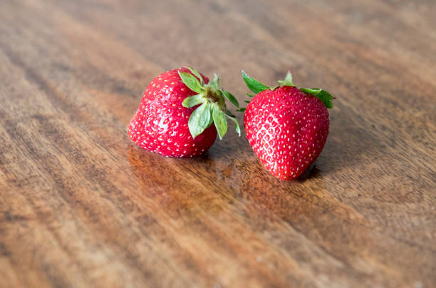 two juicy strawberries on wooden table - wet strawberry macro fruit imagens e fotografias de stock