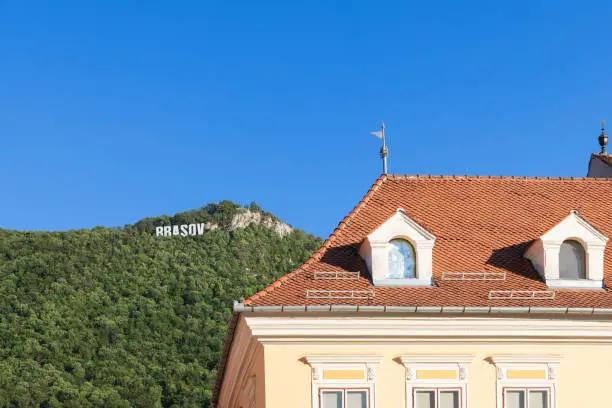 Photo of Tiled roof of 17th century Council House against the backdrop of forested hills with giant letters on the top BRASOV, Romania