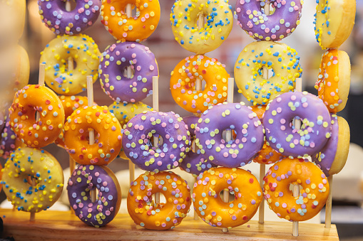 Multicolored ringed donuts with fondant icing hanging on sticks on doughnut stand, sweet food on display