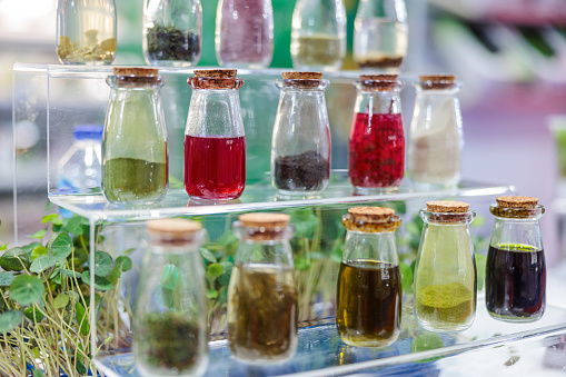 Infused olive oil of diverse colors with various herbs in small bottles with cork taps on glass shelves on display, food and healthcare