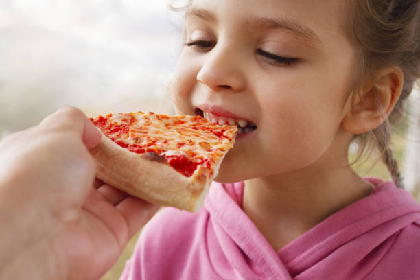 istock little girl eats pizza close up from parent's hand 1444121042