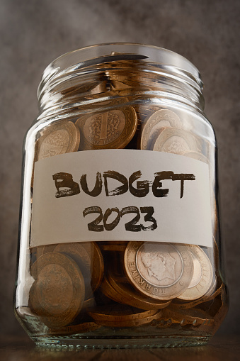 Coin savings jar with Budget 2023 text on the label filled with coins