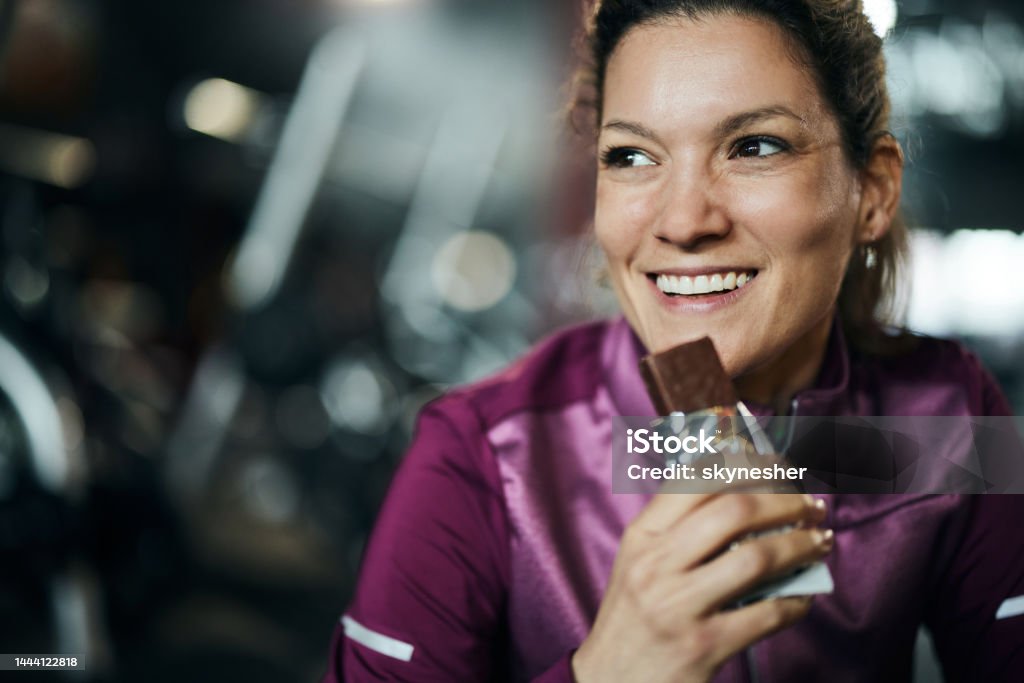 Eating protein bar on a break! Happy woman eating protein bar on a break from sports training. Eating Stock Photo