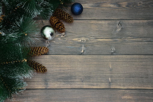 wooden board decorated with spruce branches, cones, silver and blue spheres, copy space