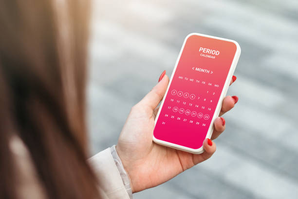 mano femenina sosteniendo un teléfono móvil con una aplicación abierta de calendario de ciclo menstrual - time month rear view calendar fotografías e imágenes de stock