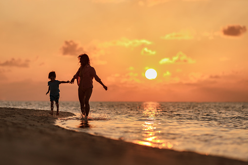 Happy mother and her small son having fun while running on the beach at sunset. Copy space.