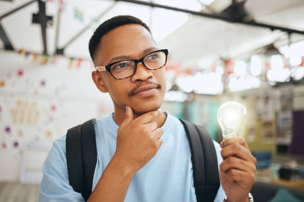 Education, thinking and man student with an idea, light bulb and innovation in a class. Vision, mission and goal by student planning and brainstorming scholarship motivation, plan success strategy
