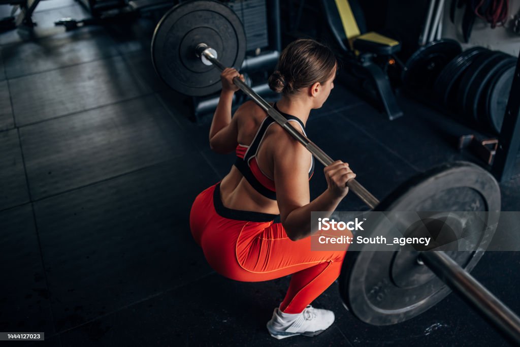 Fit woman training with weights One woman, fit young woman training with weights alone in gym. Squatting Position Stock Photo
