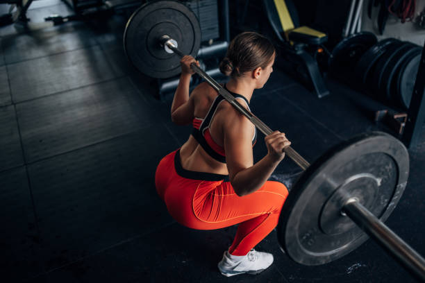 Fit woman training with weights One woman, fit young woman training with weights alone in gym. barbell back exercises stock pictures, royalty-free photos & images
