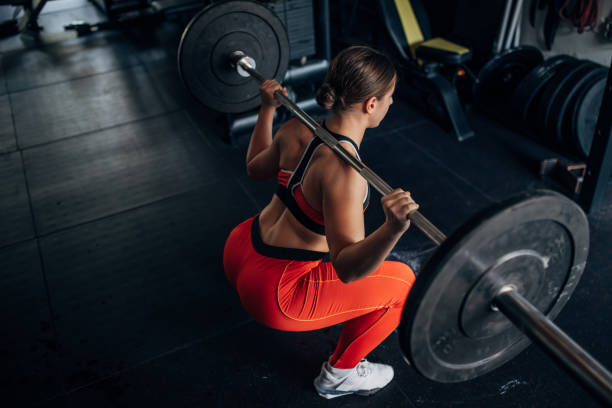 Fit woman training with weights One woman, fit young woman training with weights alone in gym. crouching stock pictures, royalty-free photos & images