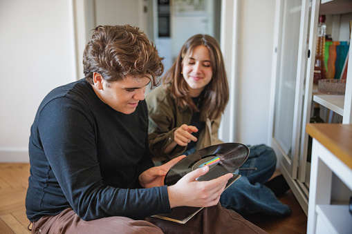 Teenage boy and girl sitting on the floor at home and discovering long play records, teens of today