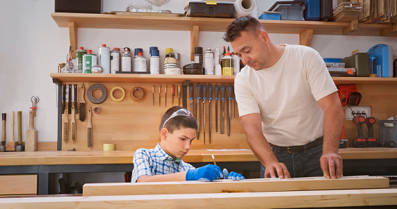 Father helping his son to mark measurement with pencil on wooden plank in workshop.