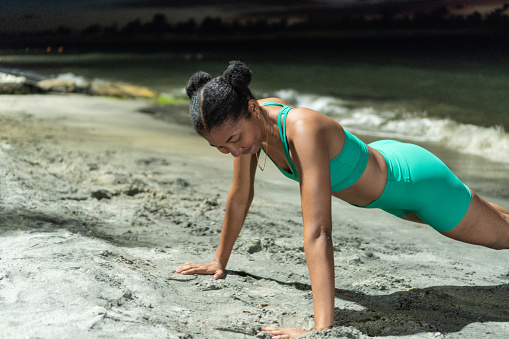 Afro woman doing push-ups on the beach