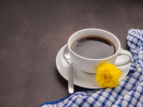 Top view of a white coffee cup with yellow flowers on a dark brown background. Space for text. Concept of beverage and relaxation.