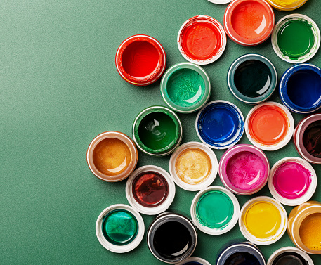 Beautiful, bright, mother-of-pearl, multicolored open cans of paint on a green background. View from above. The concept of creativity.
