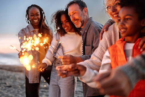 Multigenerational family using firework sparklers on the beach, having fun