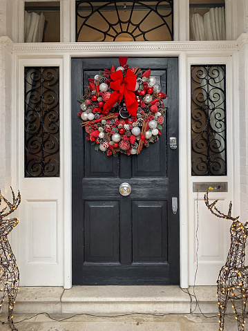 Christmas mood. Elegant christmas wreath decorated red berries, red flowers, leaves and sticks on a grey wooden door. Beautiful vintage door knocker. Christmas mood: festive christmasy themed winter natural wreath on a pink wooden door.
