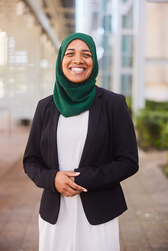 Portrait of a young muslim businesswoman wearing a hijab smiling while standing outside her office complex