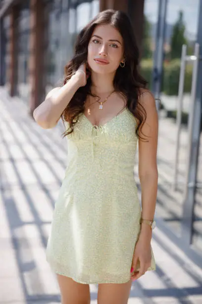 Beautiful young woman in summer dress standing outdoors on a sunny day and looking at camera with hand in hair