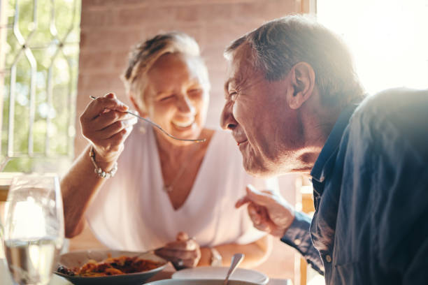 couple, love and food with a senior man and woman on a date in a restaurant while eating on holiday. travel, romance and dating with an elderly male and female pensioner enjoying a meal together - restaurant dinner dining people imagens e fotografias de stock