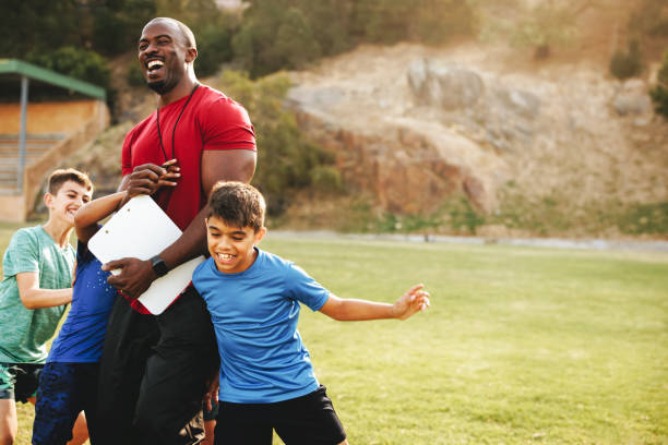 kinder, die spaß mit ihrem schultrainer haben - soccer child coach childhood stock-fotos und bilder