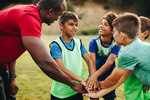 Sports trainer having a huddle with his team in a school field. Rugby coach giving his students a motivational talk before practice. Sports mentorship in elementary school.