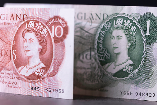 Haverfordwest, Wales - November 23, 2022: Studio shot of a detail of a UK pre-decimal ten shilling note and one pound note. These became redundant from Monday February 15th 1971 - at which date the UK changed to decimal currency. The value of the ten shilling banknote was equivalent to £0.50 in the 'new' currency. It was the smallest denomination banknote ever issued by the Bank of England.