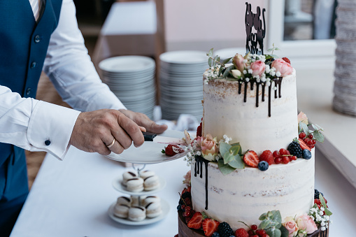 Cutting of a semi-naked cake in brown and white decorated with flowers and berries