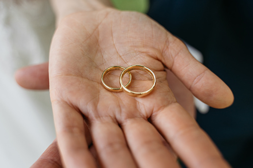 Close-up of two golden wedding rings lying on the hands of bride and groom